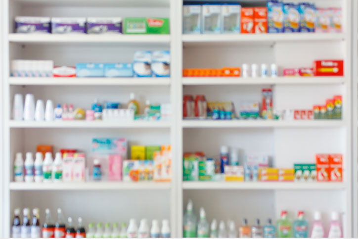 Blurred image of a pharmacy counter with shelves full of over-the-counter medications.