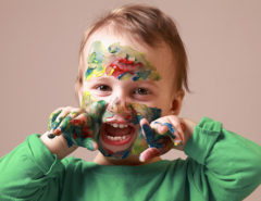 Humorous photo of cute cheerful child girl showing her hands and face painted in bright colors.