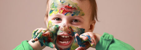 Humorous photo of cute cheerful child girl showing her hands and face painted in bright colors.