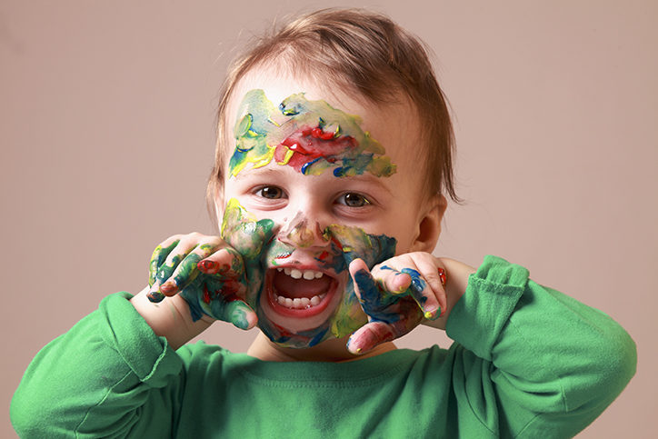Humorous photo of cute cheerful child girl showing her hands and face painted in bright colors.