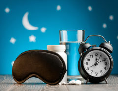 Eye mask, pills and alarm clock on a bedside table over night sky. Getting rid of insomnia, remedies for good restful sleep.