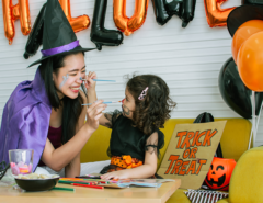 Mother an daughter in Halloween costumes painting each others faces with Halloween decorations in the background