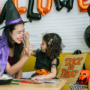 Mother an daughter in Halloween costumes painting each others faces with Halloween decorations in the background