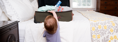 Child reaching into an open suitcase on the bed that contains medicines