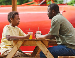 Dad talking to his son sitting at table during their rest at outdoor cafe with cold juice