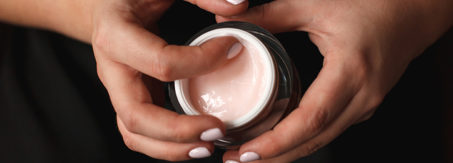 Beautiful woman hands with container of cream on dark background.