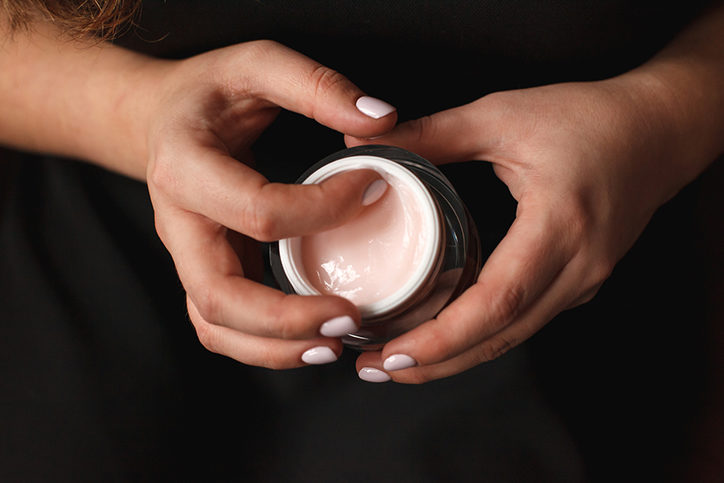 Beautiful woman hands with container of cream on dark background.