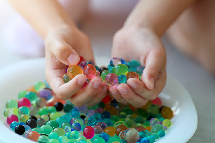 A bowl of hydrated water beads and a child's hands above holding some water beads