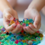 A bowl of hydrated water beads and a child's hands above holding some water beads