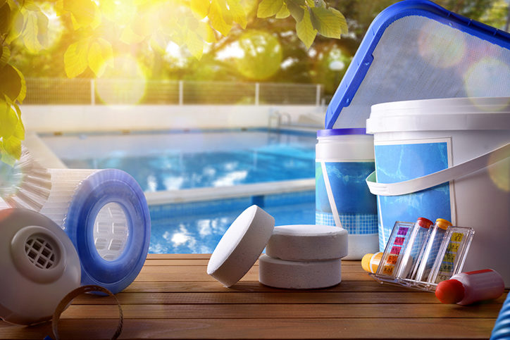 Swimming pool service and equipment with chemical cleaning products and tools on wood table and pool background. Horizontal composition. Front view