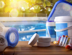 Swimming pool service and equipment with chemical cleaning products and tools on wood table and pool background. Horizontal composition. Front view