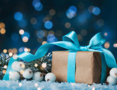 Lighted background with present wrapped in blue bow with decorative pine and white berries