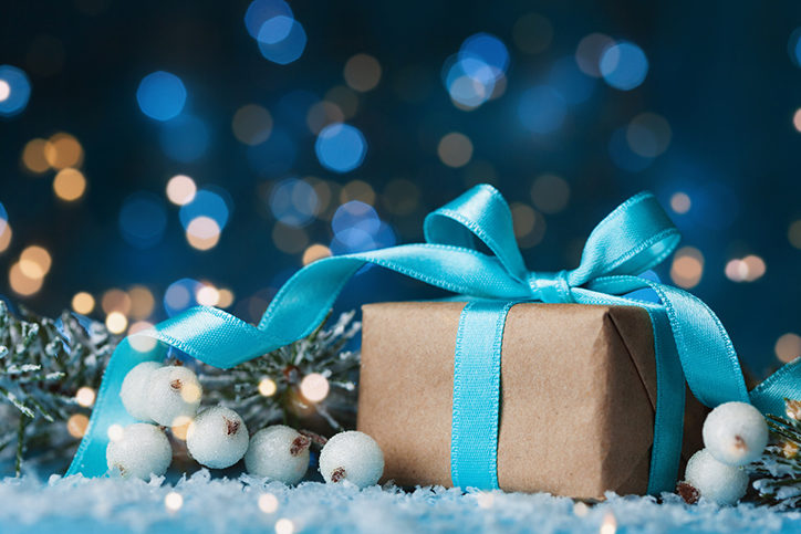 Lighted background with present wrapped in blue bow with decorative pine and white berries