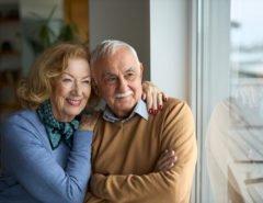 Happy senior couple looking through window at home.