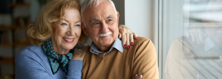 Happy senior couple looking through window at home.