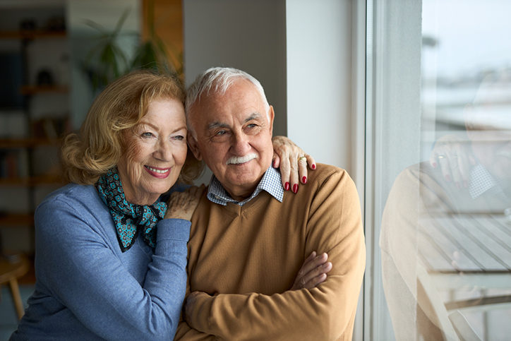 Happy senior couple looking through window at home.