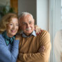 Happy senior couple looking through window at home.