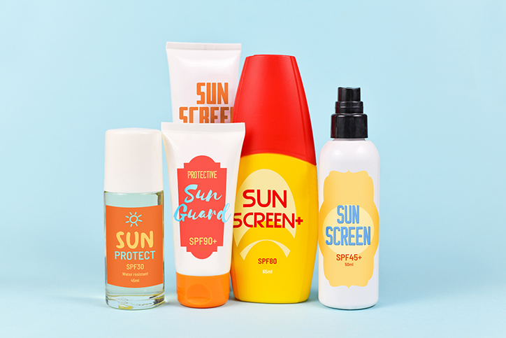 Different protective sun screen cream bottles and spray tubes with made up labels on light blue background