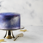 Cake with a metallic purple and blue finish sits on a cake stand.