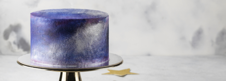 Cake with a metallic purple and blue finish sits on a cake stand.