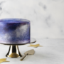 Cake with a metallic purple and blue finish sits on a cake stand.