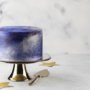 Cake with a metallic purple and blue finish sits on a cake stand.