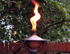 A tiki torch outdoors with a large flame coming out of the top.