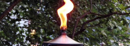 A tiki torch outdoors with a large flame coming out of the top.